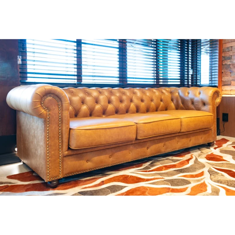 Sofá Chesterfield Zafrelli em couro caramelo em um ambiente real, com tapete e persianas.